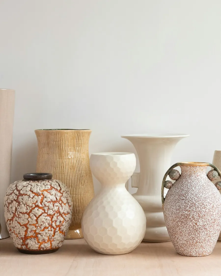 A shelf of warm, handmade ceramic vases in cream and clay tones