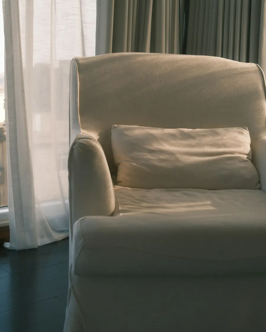 A soft white armchair beside a sheer curtain in gentle morning light
