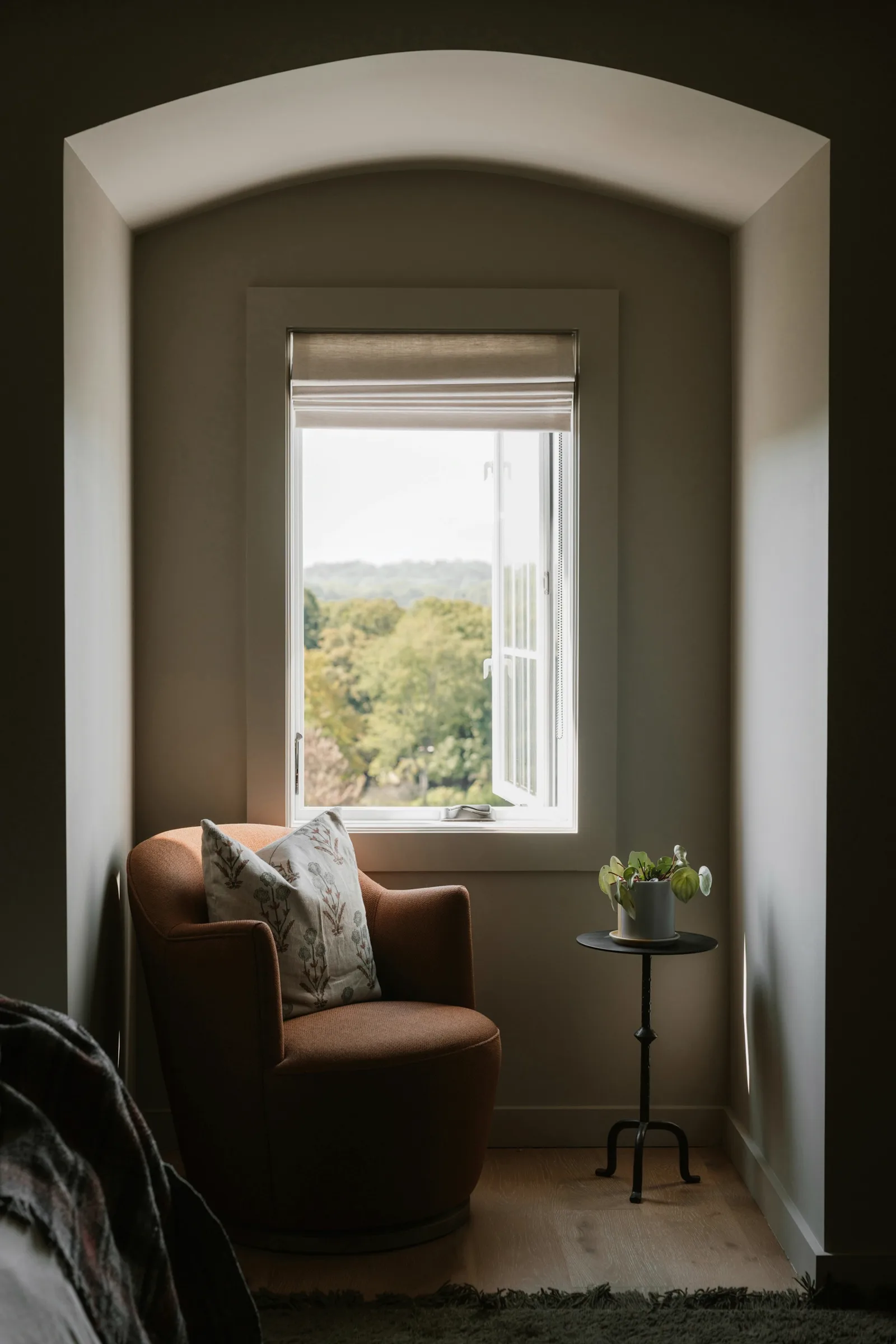 A terracotta armchair in a calm, arched window alcove with soft light and green trees beyond